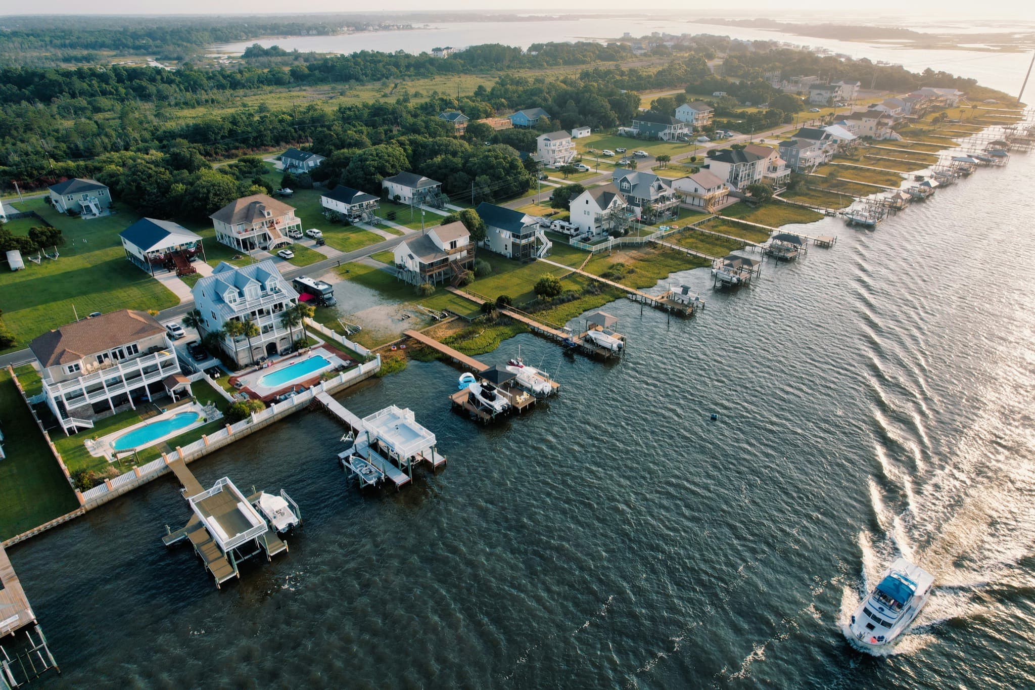 A motor yacht passing waterfront homes with private docks, boat lifts, and pools