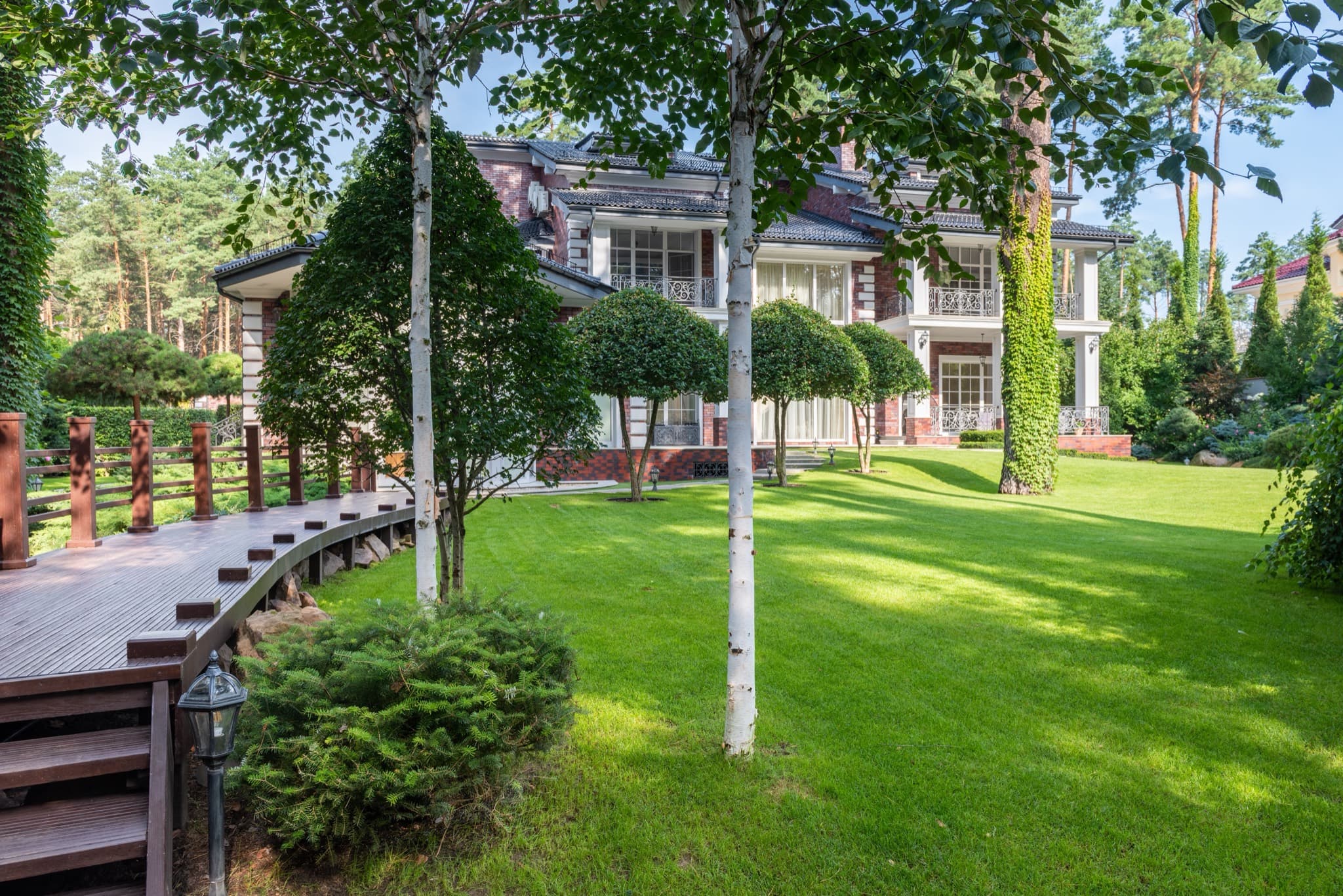 Large brick estate with a wide lawn, birch trees, and a timber boardwalk