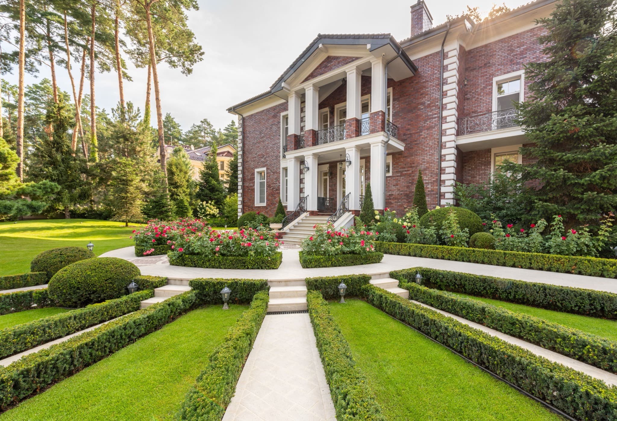 Red brick Georgian-style house with white columns, a formal boxwood garden, and tall pines