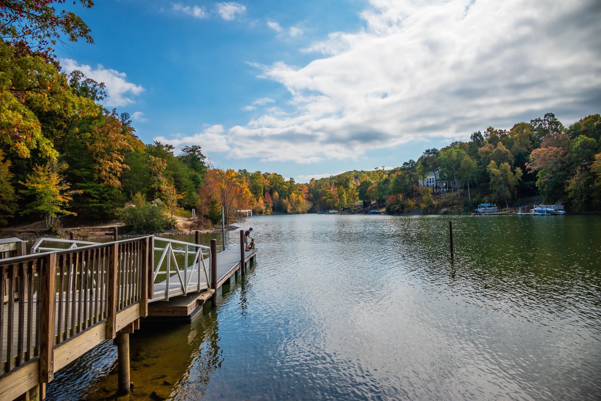 Lake cove in autumn with a wooden dock in the foreground and homes along the far shore