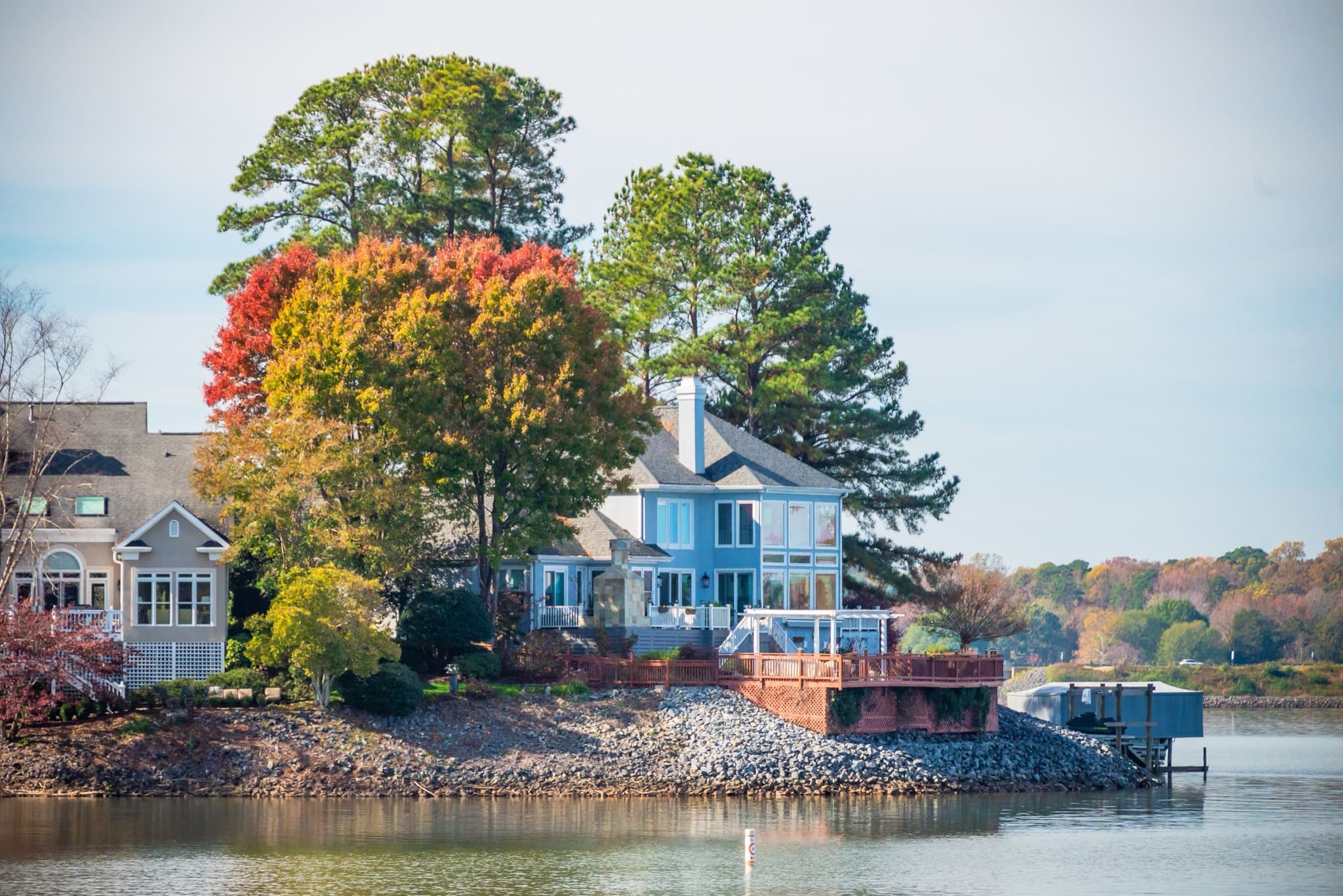Lakefront home among autumn trees, with a rock riprap shoreline and a covered boat lift