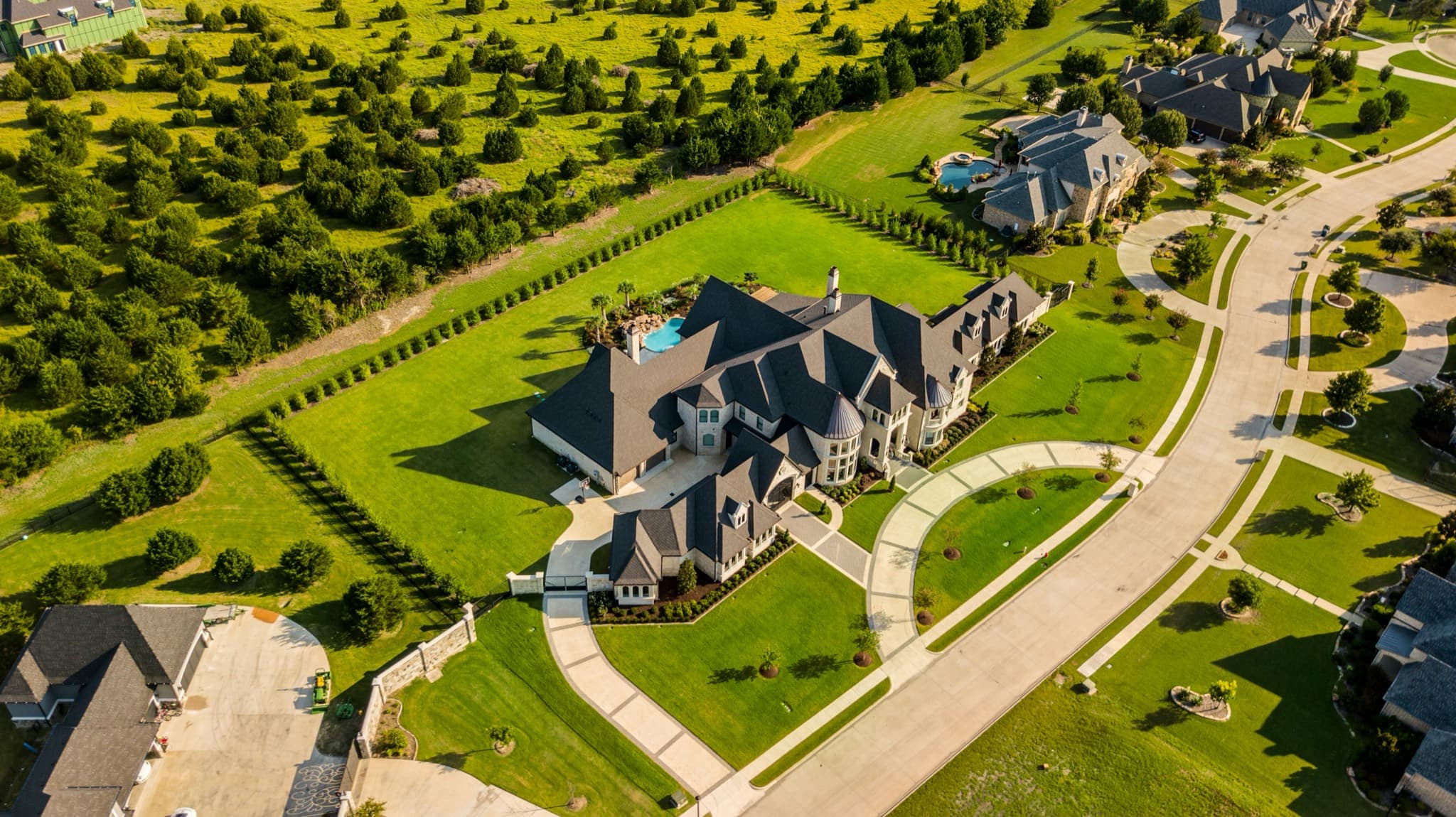 Aerial view of a large estate home with a pool, lawns, and tree-lined grounds
