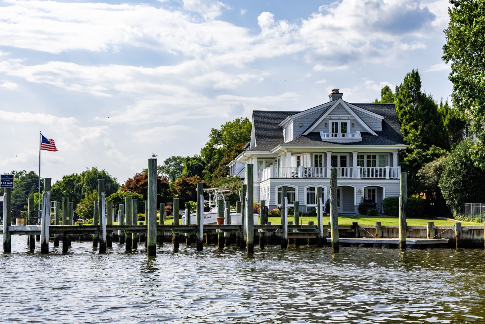 Shingle-style waterfront home with a wide porch above a row of dock pilings
